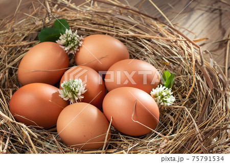 Several raw fresh chicken eggs in a nest of hay on a wooden background 75791534