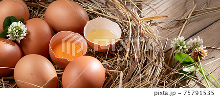 Several raw fresh chicken eggs in a nest of hay on a wooden background, horizontal banner 75791535