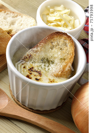 熱々のオニオングラタンスープのまわりにフランスパン、チーズ、スプーン、玉葱、ミトン 熱々のオニオングラタンスープのまわりにフランスパン、チーズ、スプーン、玉葱、ミトン 75793998