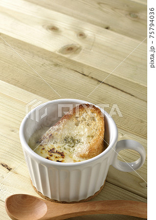 チーズに焦げ目のついてるフランスパンが入った熱々のオニオンスープと木製スプーン チーズに焦げ目のついてるフランスパンが入った熱々のオニオンスープと木製スプーン 75794036