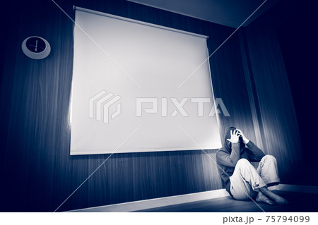depressed man sitting on floor and holding temple with his hand in dark room depressed man sitting on floor and holding temple with his hand in dark room 75794099