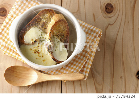 焦げ目のついたチーズ、フランスパンが入ってる熱々のオニオンスープと木製スプーンを俯瞰で撮影 75794324