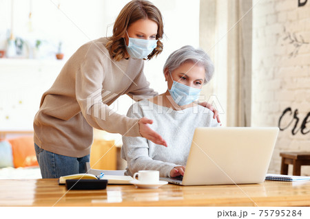 Young daughter with aged mother browsing laptop at home during COVID 19 Young daughter with aged mother browsing laptop at home during COVID 19 75795284