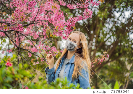 Happy woman in sakura in protective mask and smelling blooming sakura flowers after coronavirus quarantine 75798044