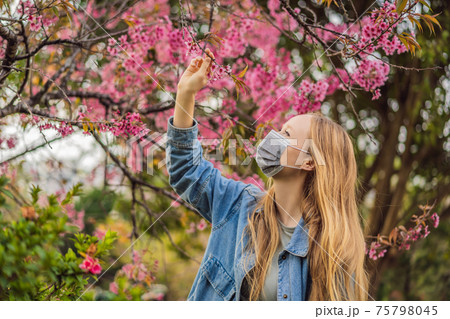 Happy woman in sakura in protective mask and smelling blooming sakura flowers after coronavirus quarantine Happy woman in sakura in protective mask and smelling blooming sakura flowers after coronavirus quarantine 75798045