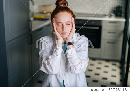 Close-up portrait of tired redhead young woman massaging temples, reducing painful head feelings 75798118