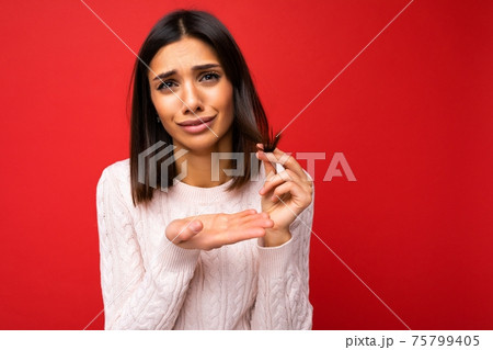 Portrait of attractive sad upset sorrowful young brunette woman wearing sweater isolated on red Portrait of attractive sad upset sorrowful young brunette woman wearing sweater isolated on red 75799405