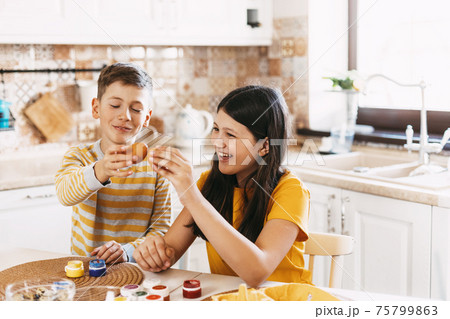 Brother and sister at home in the kitchen paint Easter eggs in different colors for Easter Brother and sister at home in the kitchen paint Easter eggs in different colors for Easter 75799863