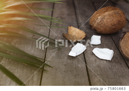 Broken coconuts on gray wooden background with palm leaf. White coconut pulp 75801663