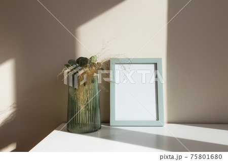Glass vase with herbarium flowers, eucalyptus branches, empty white photo frames Glass vase with herbarium flowers, eucalyptus branches, empty white photo frames 75801680