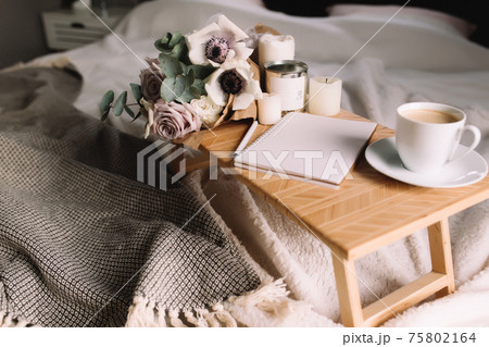 Coffee table on bed. Flowers, cup, candles, note pad, pen. Gray interior, plaid Coffee table on bed. Flowers, cup, candles, note pad, pen. Gray interior, plaid 75802164
