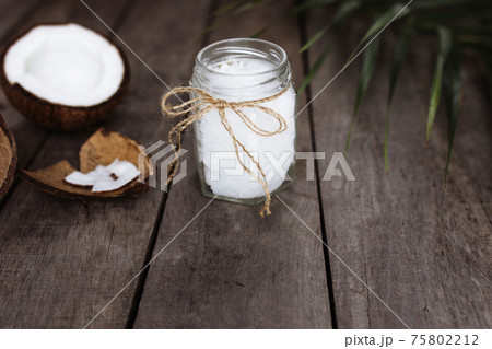 Broken coconuts on gray wooden background with oil jar. White coconut pulp Broken coconuts on gray wooden background with oil jar. White coconut pulp 75802212