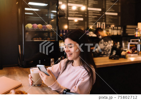 Girl smiling, drinks coffee in cafe and reading phone. Blurred background Girl smiling, drinks coffee in cafe and reading phone. Blurred background 75802712