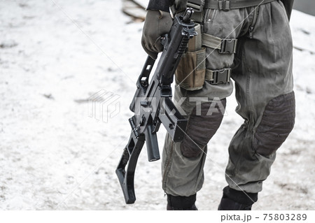 A military man with a machine gun down is walking along the road. 75803289