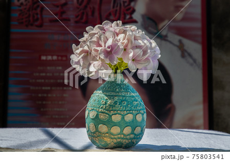 Bouquet of purple flowers in Blue handmade ceramic vase on white textured table cloth in front of Classic chinese poster movie frame. Bouquet of purple flowers in Blue handmade ceramic vase on white textured table cloth in front of Classic chinese poster movie frame. 75803541