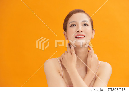 Charming woman touching her perfect soft face skin with fingers, smiling at camera over yellow background Charming woman touching her perfect soft face skin with fingers, smiling at camera over yellow background 75803753