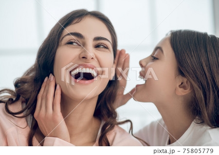 Daughter speaking in ear of laughing mother Daughter speaking in ear of laughing mother 75805779
