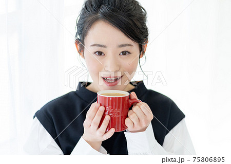 赤いマグカップでカフェオレを飲む若い女性の顔のアップ 75806895