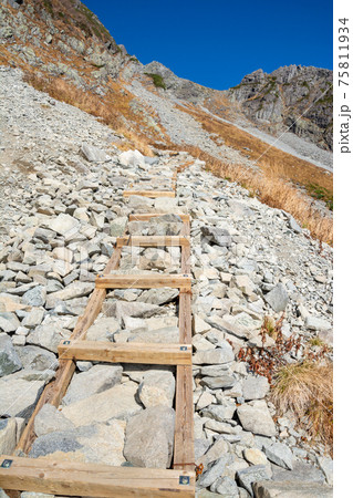 北アルプス北穂高岳山頂から涸沢への、梯子状の木材で整備された登山道。秋晴れの青空。 北アルプス北穂高岳山頂から涸沢への、梯子状の木材で整備された登山道。秋晴れの青空。 75811934