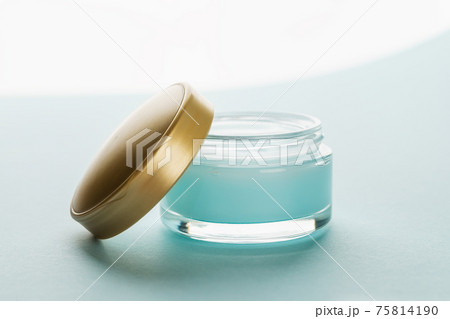 Moisturizing facial gel in an open jar with golden lid on a light blue background. Moisturizing facial gel in an open jar with golden lid on a light blue background. 75814190