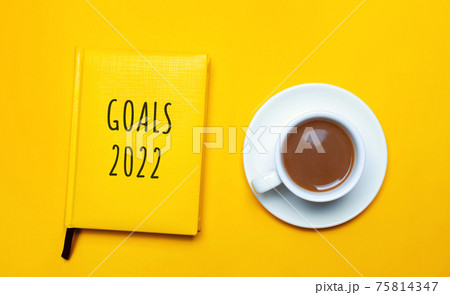 Notebook with the words Goals 2022 and a cup of coffee on a yellow background. Motivation, inspiration. Planning, plans and tasks. New business ideas. Setting goal, target. 75814347