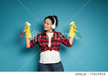 Hispanic woman, housewife, with headphones holding cleaning sprays in her hands and listening to music with her eyes closed, enjoying her homework Hispanic woman, housewife, with headphones holding cleaning sprays in her hands and listening to music with her eyes closed, enjoying her homework 75814818