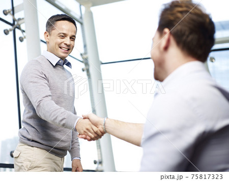 two caucasian businessmen greeting each other by shaking hands in modern office 75817323