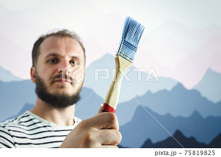 Bearded man painter holding paint brush in front of the wall. How interesting it is to paint the wall. Bearded man painter holding paint brush in front of the wall. How interesting it is to paint the wall. 75819825