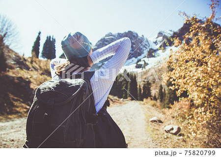 A brunette with a backpack stretches in the sun. Clear sky in the mountains. 75820799