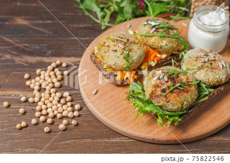 Rye bread sandwiches with chickpea cutlets and vegetable salad. On a wooden board with sauce. And chickpeas on the table. Rye bread sandwiches with chickpea cutlets and vegetable salad. On a wooden board with sauce. And chickpeas on the table. 75822546