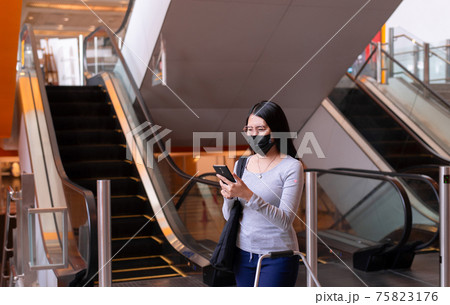 Asian woman wearing face mask and using mobile phone during coronavirus pandemic in the mall Asian woman wearing face mask and using mobile phone during coronavirus pandemic in the mall 75823176