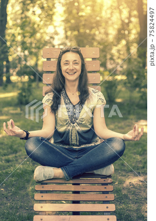 smile girl doing yoga and meditating in the city park on a sunny day. Sitting on a wooden bench. toned 75824497