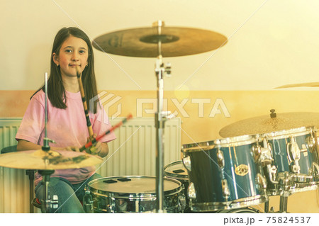 Happy girl in music therapy by playing drum kit on music room. Beautiful young girl drummer with drumsticks playing drums and cymbals. Female drummer. toned Happy girl in music therapy by playing drum kit on music room. Beautiful young girl drummer with drumsticks playing drums and cymbals. Female drummer. toned 75824537