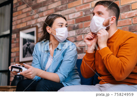 Close-up portrait of happy young couple wearing medical protective masks playing video games on console 75824959