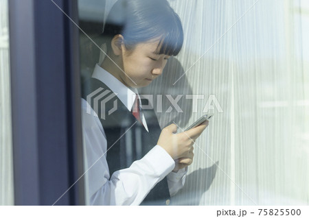 窓辺でスマートフォンを見る中学生（外出自粛要請のイメージ） 75825500