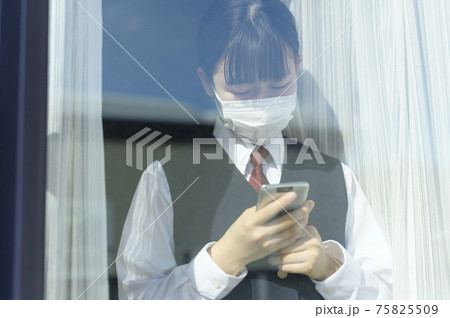 窓辺でスマートフォンを見る中学生（外出自粛要請のイメージ） 75825509
