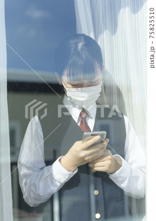 窓辺でスマートフォンを見る中学生（外出自粛要請のイメージ） 75825510