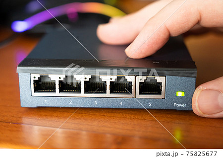 Close-up image of a router being put into service: the hand connects the power cable on the back, the green light turns on . Close-up image of a router being put into service: the hand connects the power cable on the back, the green light turns on . 75825677