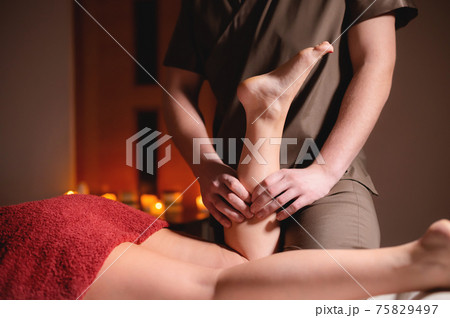 Male masseur doing massage of legs and calves in the dark room of the massage room Male masseur doing massage of legs and calves in the dark room of the massage room 75829497