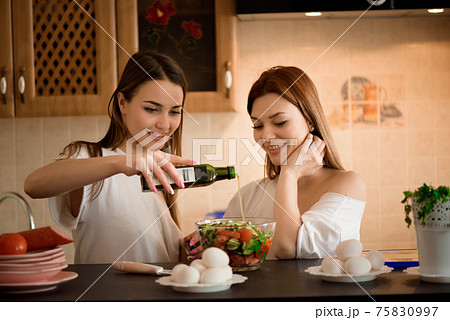 Smiling sisters preparing dinner together in the kitchen. Smiling sisters preparing dinner together in the kitchen. 75830997