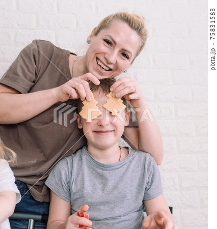 happy mom and her son play together while making cookies in the kitchen. mom covers baby s eyes with freshly made cookies happy mom and her son play together while making cookies in the kitchen. mom covers baby s eyes with freshly made cookies 75831583