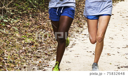 Legs of two girls running side by side on a dirt path 75832648