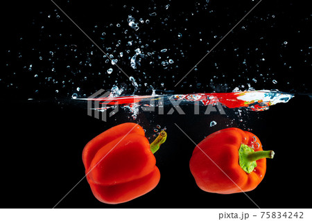 Bell pepper falling into water with a splash against black background 75834242