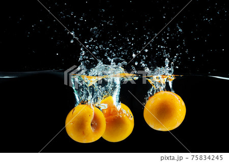 Three yellow plums diving into the water against black background Three yellow plums diving into the water against black background 75834245