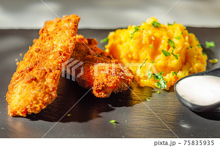 Breaded and herbed chicken breast fillet served with mashed carrots with potatoes  and  tomato salad with onions 75835935