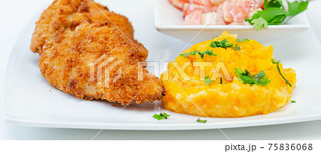 Breaded and herbed chicken breast fillet served with mashed carrots with potatoes  and  tomato salad with onions 75836068