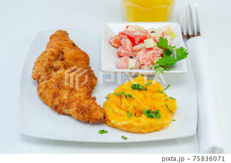 Breaded and herbed chicken breast fillet served with mashed carrots with potatoes  and  tomato salad with onions 75836071