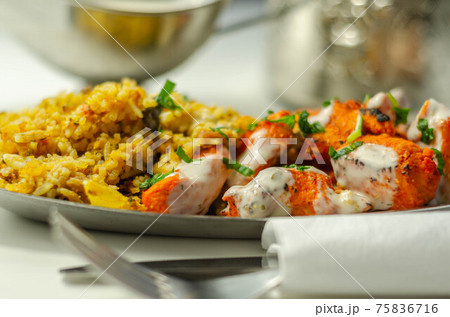 Pieces of cooked marinated chicken breast in an onion and tomato sauce with yogurt and mint and crispy fried onions layered with spiced basmati rice 75836716