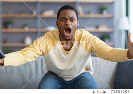 Furious black guy watching football game on TV Furious black guy watching football game on TV 75837202