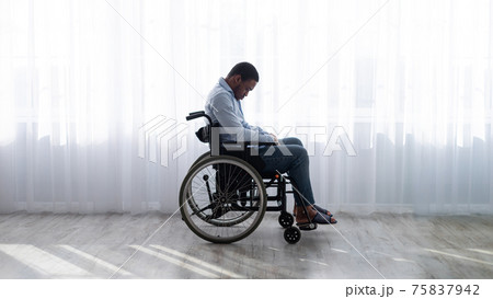 Full length of handicapped black man in wheelchair feeling desperate and lonely, suffering from depression indoors Full length of handicapped black man in wheelchair feeling desperate and lonely, suffering from depression indoors 75837942